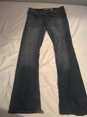 Blå bootcut jeans från ONLY - Säljer ett par blå bootcut jeans från ONLY med klassisk femficksdesign och dragkedjegylf. Jeansen har slitningar och lätt tvättad look, samt råa kanter nertill. Perfekta för en avslappnad och trendig stil. Dragkedjan är sönder går säkert att fixa.