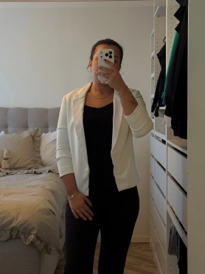 Vit kavaj med öppen front - Stilren vit kavaj med öppen front och trekvartsärmar. Kavajen har en mjuk, något stretchig passform och saknar knappar för en avslappnad look. Perfekt att slänga över en topp för en clean och modern stil.