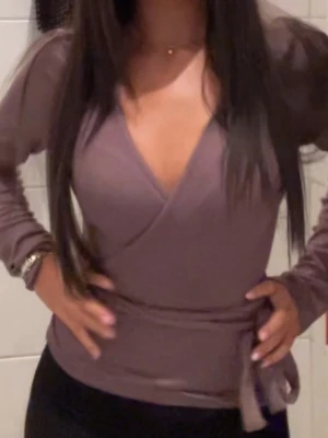 brun omlottopp med knytband - Trendig  brun omlottopp med långa ärmar och knytband i midjan. Djup v-ringning framtill ger en snygg och modern look. Perfekt att styla med både jeans och kjol. Använd endast 1 gång. Skriv för fler bilder