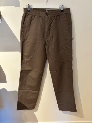 Bruna linnebyxor från ARKET med resårmidja - Snygga bruna linnebyxor med avslappnad passform och resår i midjan. Byxorna har snedställda fickor fram och två passpoalfickor bak. Perfekta för en chill och stilren look. Tillverkade i ett lätt och luftigt linnematerial.