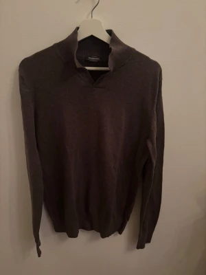 Mörkbrun stickad tröja med krage - Snygg mörkbrun stickad tröja från Dressmann med hög ribbad krage och långa ärmar. Tröjan har en enkel, stilren design och är perfekt för lager på lager. Materialet ser ut att vara mjukt och bekvämt, passar till många olika outfits.