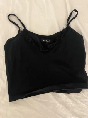 Svart spetsdetaljerad linnetopp - Snygg svart linnetopp från Even&Odd med tunna axelband och spetsdetaljer längs urringningen. Perfekt att styla med jeans eller kjol för en trendig look. Materialet känns mjukt och lätt mot huden.