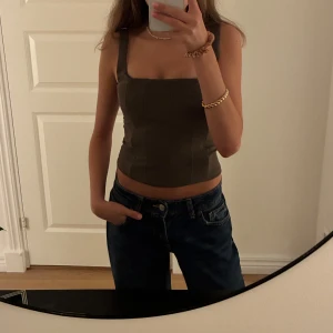 Olivgrön korsett-topp - Säljer en olivgrön korsett-topp med breda axelband och fyrkantig urringning från zara.Använd 1 gång innan.