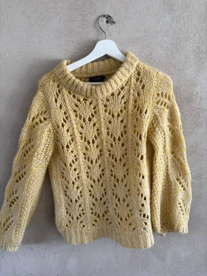 Gul stickad tröja med hålmönster - Snygg gul stickad tröja från MONKI med trendigt hålmönster och bred ribbad kant vid hals, ärmslut och nederkant. Tröjan har en avslappnad passform och är perfekt för dig som gillar en mysig men ändå stilren look. Materialet känns mjukt och fluffigt.