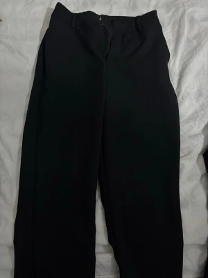 Svarta vida kostymbyxor från bikbok - Säljer ett par svarta kostymbyxor med hög midja och vida ben. Byxorna har hällor för skärp och stängs med dragkedja fram. Perfekta för en clean och stilren look.