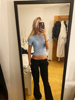 Ljusblå stickad croppad topp - Säljer en ljusblå stickad croppad topp med korta ärmar och vågig kant nertill. Toppen har ett luftigt, virkat mönster och är ganska stretchig i materialet. 