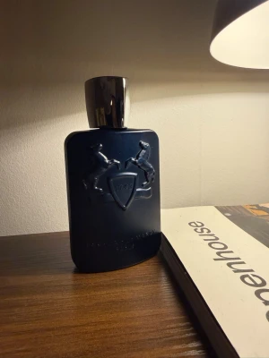 Parfums de Marly Layton parfym - Mörkblå parfymflaska från Parfums de Marly med silverfärgat lock. Flaskan har en elegant matt finish och är dekorerad med två upphöjda hästar och en sköld med siffran 1743. Lyxig och stilren design som sticker ut på hyllan.