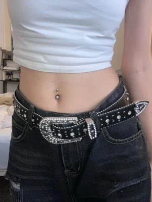 Svart Y2K bälte med silverdetaljer - Snyggt svart bälte med glittriga silverdetaljer och nitar längs hela bandet. I bra skick, 112 Cm långt 