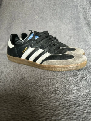 Adidas Samba OG – Black / White – Gum Sole - Klassiska Adidas Samba sneakers i svart med vita tre ränder och klassisk gum sole.  En ikonisk modell inspirerad av retro football och terrace culture, vilket gör dem väldigt populära igen.  Detaljer • Adidas Samba • Svart / vit färg • Klassisk gum sole • Retro terrace style • Bekväma och slitstarka  Perfekta till jeans, cargos eller casual outfits.  📦 Skickas snabbt 💬 Hör av dig vid frågor
