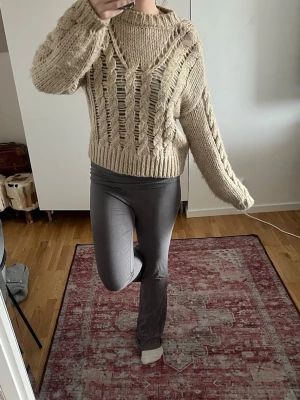 Beige chunky stickad tröja - Chunky stickad tröja i beige med grova maskor och hålmönster framtill. Tröjan har breda ärmar, ribbade muddar och en avslappnad passform. Perfekt för lager på lager och en cool, avslappnad stil. Pris kan diskuteras🩷