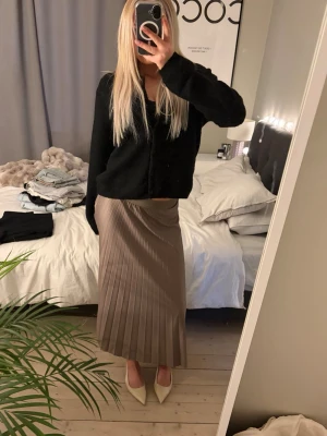 Brun långkjol från Vila - Snygg siden långkjol från Vila i en mjuk brun nyans. Kjolen har ett brett midjeband och ett glansigt, flowy tyg som ger en lyxig känsla. Perfekt för dig som gillar stilrena och trendiga plagg.