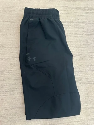 Svarta mjukisbyxor från Under Armour - Snygga svarta mjukisbyxor från Under Armour med elastisk midja och diskret logga på benet. Byxorna har raka ben och är tillverkade i ett mjukt, stretchigt material som passar perfekt för chill eller träning. Klassisk och clean look som funkar till det mesta. Köpt för 750 på hemsidan Under armour