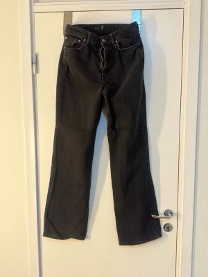 Svarta raka jeans från Gina Tricot - Säljer ett par svarta jeans från Gina Tricot med rak passform och hög midja. Jeansen har klassiska fem fickor, bälteshällor och knappgylf. Materialet är kraftig denim i bomull som ger en snygg vintagekänsla.