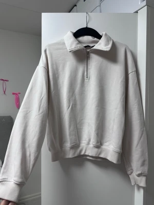 Beige halvzip sweatshirt - En stilren beige sweatshirt med halvzip och krage. Tröjan har långa ärmar, ribbade muddar och avslut. Tillverkad i mjukt bomullsliknande material som känns skönt mot huden. Perfekt för en avslappnad och trendig look. Färgen är gräddvit.