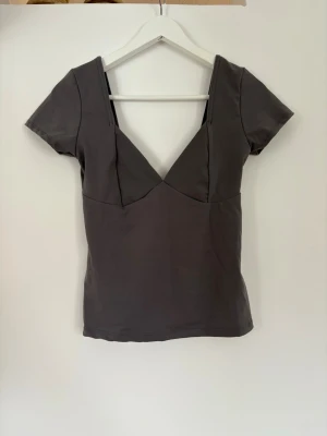 Grå topp - En grå, kortärmad topp som passar perfekt till vardag & fest. V ringad framtill och djup rygg. Från Amisu, mycket gott skick, storlek M. Silikonband längst hela urringningen för att den ska sitta uppe bättre🤗