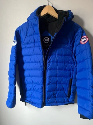 Blå dunjacka från Canada Goose - säljer nu min blå dunjacka från Canada Goose med huva och svarta detaljer. youth storlek L (14-16). Nypris 5000