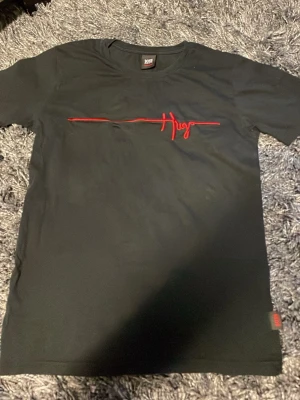 Svart Hugo Boss t-shirt med röd logga - Snygg svart t-shirt från Hugo Boss med rakt snitt och röd broderad Hugo-logga över bröstet. 