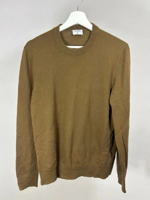 Filippa K Stickad Tröja | M - Klassisk brun stickad tröja från Filippa K med rund halsringning och ribbade muddar vid ärmslut och nederkant. Enkel och stilren design som passar perfekt till jeans eller chinos. Tillverkad i mjukt material för en bekväm känsla.