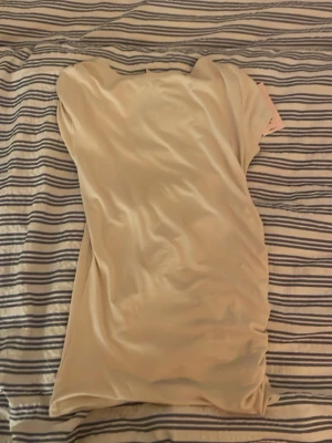 Champagnefärgad T-shirt Nelly - Snygg champagnefärgad tröja från Nelly i ett glansigt satinliknande material. Klänningen har enkel, rak passform och korta ärmar. Perfekt för dig som gillar stilrena och eleganta plagg.