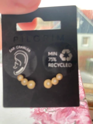 Guldiga ear crawler örhängen Pilgrim - Snygga ear crawler örhängen från Pilgrim med tre små guldfärgade pärlor på varje örhänge. Tillverkade av minst 75% återvunnet material. Perfekta för dig som gillar trendiga och stilrena accessoarer.