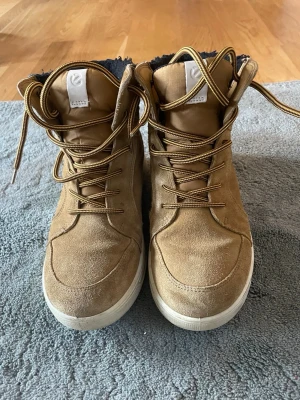Bruna stövletter från Ecco Gore-Tex - Snygga bruna stövletter från Ecco med Gore-Tex, perfekta för kalla dagar. Ovandel i mocka och textil, fodrade med svart mjukt material. Klassisk snörning och vit sula ger en sportig look. Märket syns på sidan och plösen.