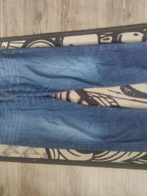 Blå raka jeans med slitningar - Snygga blå jeans med raka ben och slitningar på låren. Klassisk femficksmodell med knapp och dragkedja framtill. Jeansen har en tvättad look och är gjorda i denim, perfekt för en avslappnad stil.