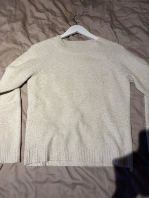 Beige stickad tröja Vero Moda - Mysig beige stickad tröja från Vero Moda med rund halsringning och långa ärmar. Tröjan har ribbade muddar vid ärmslut och nederkant, vilket ger en klassisk och enkel look. Perfekt för lager på lager under kyliga dagar.