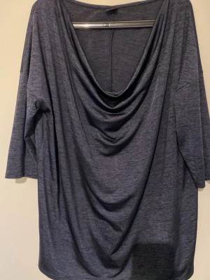 Mörkblå draperad topp Gina Tricot - Snygg mörkblå topp från Gina Tricot med draperad framsida och lös passform. Toppen har trekvartsärm och ett mjukt, stretchigt material som känns skönt mot huden. Perfekt för dig som gillar en avslappnad men ändå stilren look.