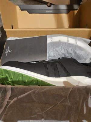 Svarta arbettskor från Xelar strl 43 - Säljer ett par svarta arbetsskor strl 43 från Xelar med gröna detaljer på sulan och tåpartiet. Skorna har sportig look, snabbsnörning och meshpartier för bra ventilation. Sulan är vit med grön undersida och skon har dragflik bak för enkel påtagning. Medföljer ett par sulor även dom oanvända strl 40-42. Ord pris på bara sulorna ca 600 :-