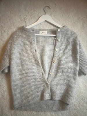 Grå ribbad kofta från Gina Tricot - Mysig grå kofta från Gina Tricot i ullblandning. Kortärmad modell med ribbad struktur och knappar framtill. Perfekt att slänga över en topp för en chill look.köpt för 329kr 