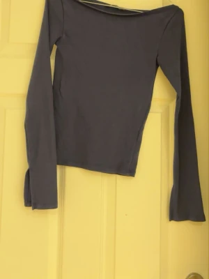 Mörkblå långärmad topp med slits boatneck  - En stilren mörkblå långärmad topp med slits vid ärmsluten. Toppen har en rak passform och är tillverkad i mjukt bomullsmaterial. Perfekt för dig som gillar minimalistisk och clean stil.