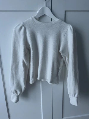Vit tröja med puffärmar - Säljer en stilren vit tröja med puffärmar och rund hals. Tröjan har en mjuk, strukturerad yta och ribbade muddar vid ärmsluten. Perfekt för dig som gillar trendiga detaljer och enkel design.