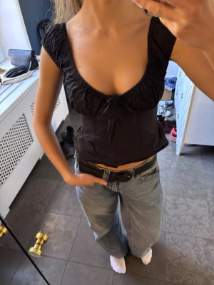 Svart linnetopp med knyt fram - Svart linnetopp med djup urringning och knyt fram. Toppen har en figurnära passform och är ärmlös.