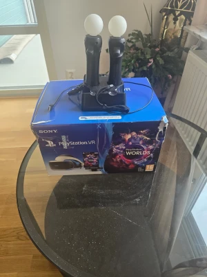 PlayStation VR med Move-kontroller - PlayStation VR-headset med två svarta PlayStation Move-kontroller och laddningsstation. Paketet inkluderar originalkartong och spelet PlayStation VR Worlds. Perfekt för dig som vill uppleva VR på PlayStation.