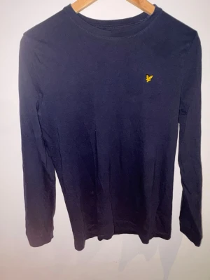 Lyle & Scott - Mörkblå långärmad tröja från Lyle & Scott. Riktigt sexig passning på denna. Storlek 14-15 år, motsvarar S.