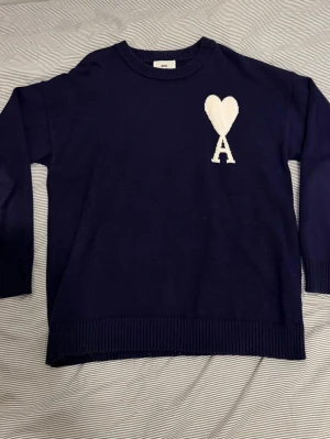 Ami Paris stickad tröja L/XL - Fin stickad tröja från ami Paris i storlek L/XL.  Sparsamt använd och i mycket bra skick. Marinblå kulör med vit logotyp. Hör av dig vid minsta fråga!