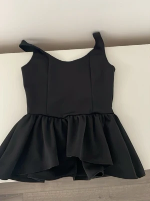 Svart volangklänning från NA-KD - Supersnygg svart klänning från NA-KD med volangkjol och breda axelband. Klänningen har en figurnära överdel och en utställd kjol med lager av volanger. Perfekt för dig som vill sticka ut med en stilren look.