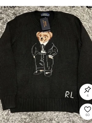 Svart stickad tröja Polo Bear - Svart stickad tröja från Polo Ralph Lauren med ikoniska Polo Bear-motivet framtill. Tröjan har rund halsringning, ribbstickade muddar och RL-broderi vid nederkanten. Perfekt för dig som gillar klassisk och lekfull stil.