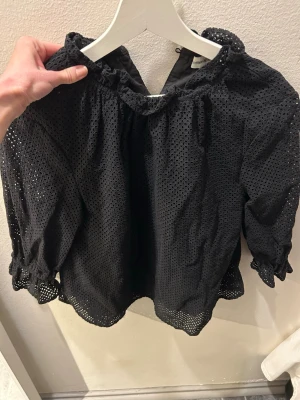 Svart broderad blus från Carin Wester - Snygg svart blus från Carin Wester i storlek 36. Blusen har broderade hål, volangkant vid halsen och ärmslut samt puffiga långärmar. Säljer då den ej kommer till användning. 🩷