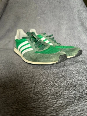 Adidas Retro Runner Sneakers – Green / White - Klassiska Adidas retro sneakers i grön färg med vita tre ränder.  Inspirerade av äldre Adidas running-modeller, vilket ger en riktigt snygg vintage sneaker look.  Detaljer • Adidas • Grön / vit färg • Klassisk 3-stripe design • Retro running style • Bekväma vardagssneakers  Perfekta till jeans, cargos eller casual outfits.  📦 Skickas snabbt 💬 Hör av dig vid frågor