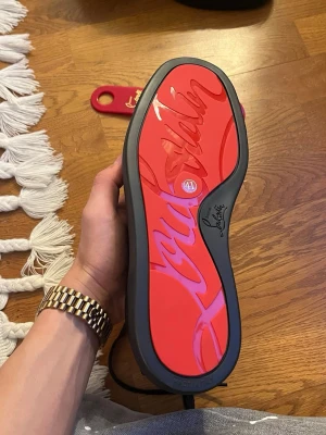 Christian Louboutin - Snygga svarta sneakers från Christian Louboutin med ikonisk röd sula och diskret logga på sidan. Skorna har snörning och är tillverkade i mocka med detaljer i syntet. Perfekta för dig som vill sticka ut med exklusiv streetstyle.