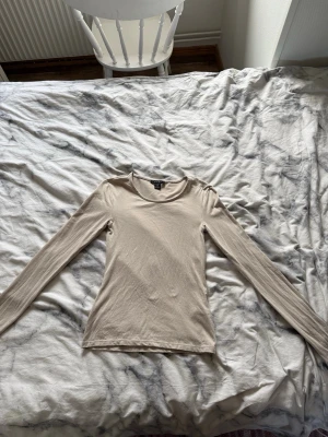 Beige långärmad topp från Amisu - En stilren beige långärmad topp från Amisu i mjuk bomull. Toppen har rund halsringning och en slim passform som sitter snyggt på kroppen. Perfekt att matcha med jeans eller kjol för en enkel och clean look.