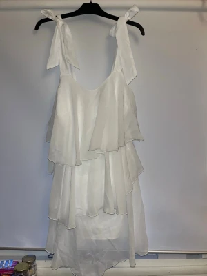 Vit volangklänning från Bubbleroom - Superfin vit klänning från  Vero Moda/Bubbleroom med volanger i flera lager och knytband på axlarna. Klänningen är kort och har en luftig känsla, perfekt för varma dagar. Tillverkad i ett lätt och skönt material som ger en flowy look. Helt ny med alla lapparna kvar