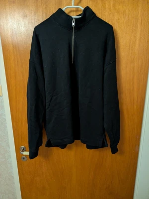 Svart half-zip hoodie Abercrombie - Svart oversized hoodie från Abercrombie & Fitch med halv dragkedja och hög krage. Tillverkad i mjukt material, perfekt för en chill och avslappnad stil. Klassisk design utan tryck eller mönster, passar till det mesta.