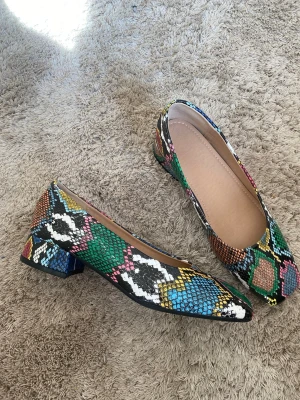 Färgglada pumps med ormmönster - Unika pumps med blockklack och färgstarkt ormskinnsmönster i grönt, blått, gult, rosa och svart. Skorna har kantig tå och låg klack, tillverkade i syntetmaterial. Perfekta för dig som vill sticka ut med din stil. Stl 38 oanvända