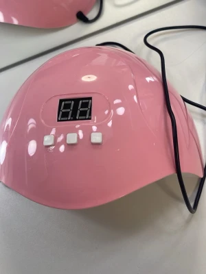 Rosa LED UV-lampa för naglar - Snygg rosa LED UV-lampa för naglar med digital display och tre vita knappar för timerinställning. Lampan har flera inbyggda LED-lampor på insidan och är perfekt för att härda gel- och shellacklack. Kopplas in med sladd. Modern och smidig design.