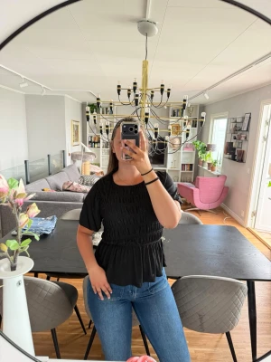 Svart blus från Lindex - Supersöt svart blus från Lindex med smockad midja och puffiga korta ärmar. Blusen har rund halsringning och volang nertill. Aldrig använd🖤