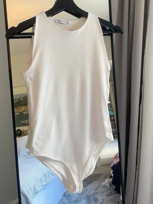 Vit ärmlös topp från Stradivarius - Vit body från Stradivarius i storlek L (Men sitter som S). Bodyn har ärmlös design, rund halsringning och knäppning i grenen. Tillverkad i mjukt och stretchigt material som sitter snyggt på kroppen. Köpt i Italien. Använd 1 gång, finns mindre nästan osynlig smutsfläck på den, men tror den går att få bort med blekmedel. Köpt för cirka 200kr säljer för 99kr.