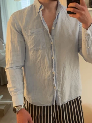 Ljusblå skjorta med knappar - Snygg ljusblå skjorta med klassisk krage och bröstficka. Skjortan har långa ärmar och knäppning framtill. Perfekt för en stilren och avslappnad look.