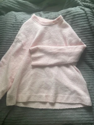 Ljusrosa stickad tröja - Mysig ljusrosa stickad tröja med rund halsringning och ribbade muddar vid ärmslut och nederkant. Tröjan har en avslappnad passform och är perfekt för att hålla värmen under kyliga dagar.